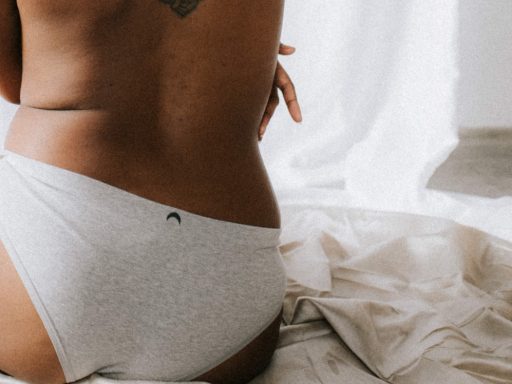 person wearing gray underwear with tribal back tattoo sitting on bed