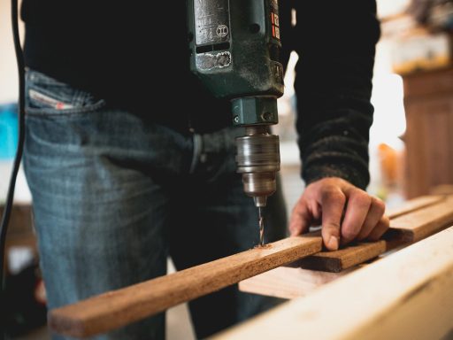 Close-up of a person using an electric drill on a wooden plank, showcasing detailed woodworking skills.